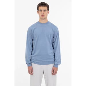 A light blue long sleeve crewneck tee featuring a logo on the front, styled with grey sweatpants.