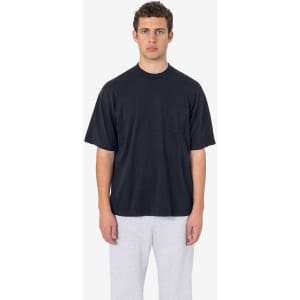 A black short sleeve pocket tee with a relaxed fit and a casual style, worn with grey pants. The shirt features a logo.