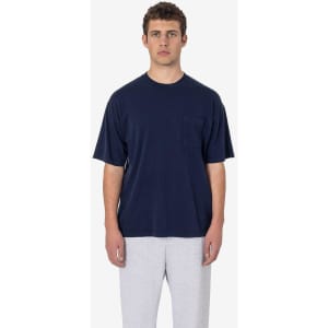 A model wearing a navy short sleeve garment-dyed pocket tee paired with grey sweatpants. The shirt features a pocket and has a logo.