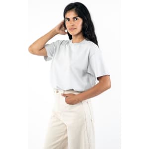 A wide tee in light grey, featuring a relaxed fit and short sleeves, worn with high-waisted trousers. It has a logo.