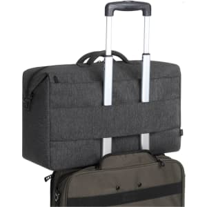 A grey duffle bag with a retractable handle, resting on top of a black suitcase. Features branding.