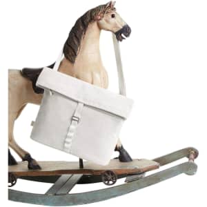 A cream coloured satchel bag with a flap and strap, displayed next to a rocking horse. The bag features a logo.