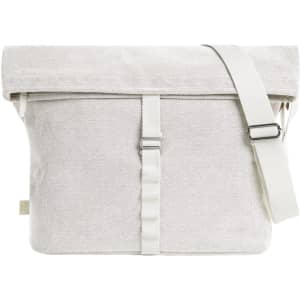 A light grey satchel bag with a roll-top closure and adjustable shoulder strap, featuring a branded logo.