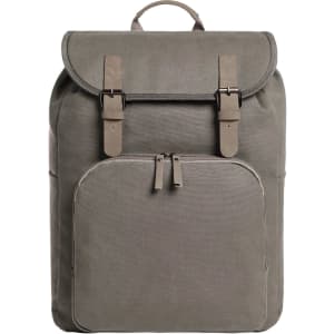 A grey backpack with a fold-over top, buckle straps, and a front zip pocket. It features a logo on the side.