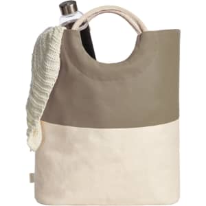 A tote bag in beige and olive green, featuring a circular handle and a drink bottle inside, with a knitted item draped over it.