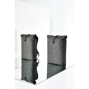 A grey roller backpack with a fold-over top and shoulder straps, displayed against a reflective surface.
