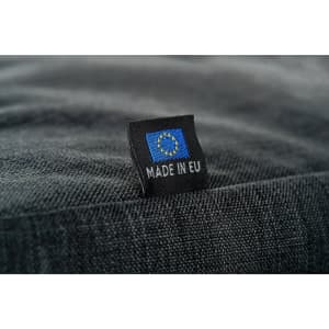A close-up of a textured black fabric bag showcasing a small tag with a logo and "MADE IN EU".