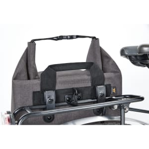 A grey cycle bike bag with a handle and fastening, attached to a bike rack. It has a sturdy design and a logo.