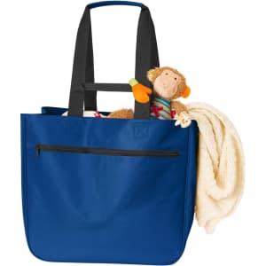 A blue tote bag with black straps, filled with a plush monkey toy and a cream-coloured blanket.