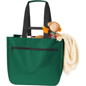 A green tote bag with black handles contains a plush monkey toy and a beige blanket. It has a front zip pocket.