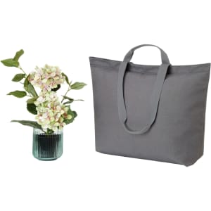 A grey tote bag with two long handles beside a vase with decorative flowers. The bag features a logo.