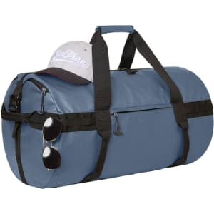 A blue duffle bag with black straps, a grey cap resting on top, and sunglasses attached to the side.