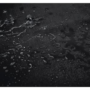 A close-up of a textured black surface with water droplets scattered across it.
