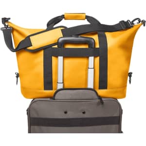 A yellow duffle bag with black straps sits atop a grey suitcase, featuring a logo on the bag.