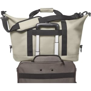 A beige duffle bag with black straps, featuring a retractable handle and a zipped compartment. Includes a branding logo.