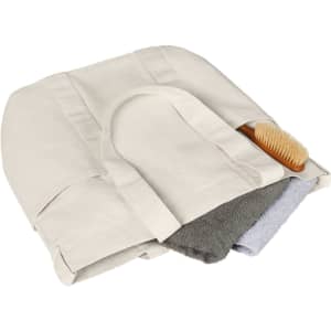 A beige tote bag filled with a grey towel and a small wooden brush, featuring a logo.