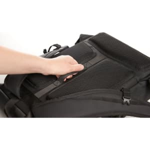 A black laptop backpack with padded straps and a handle is held by a hand, featuring a structured back panel.
