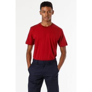 A model wearing a red short sleeve fine jersey crew tee paired with navy trousers, featuring a logo on the shirt.