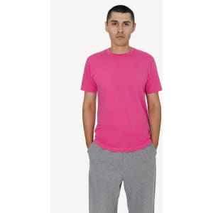 A model wearing a pink short sleeve fine jersey crew tee paired with grey trousers. The tee features a logo.