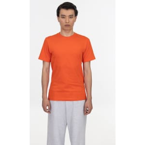 An orange short sleeve fine jersey crew tee displayed on a model wearing grey pants, featuring a logo.