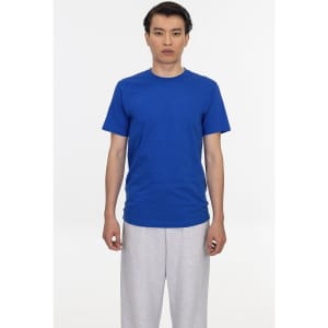 A blue short sleeve fine jersey crew tee on a model, paired with grey sweatpants. The shirt features a logo.
