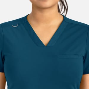 A teal women's banded V-neck top featuring a subtle pocket and a logo on the shoulder.