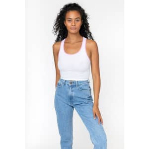 A woman models a white rib crop tank top with pink accents, paired with high-waisted blue jeans. The top features a logo.