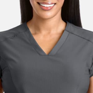 A model wearing a grey banded V-neck top, showcasing a simple and elegant design. The top features a logo.