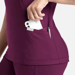 A close-up of a woman wearing a burgundy banded V-neck top, placing a phone into a side pocket.