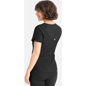 A woman is wearing a black Embrace Luna Tuckable Y-Neck Top, viewed from the back. The top features a logo.