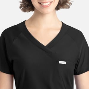 A black Y-neck top featuring a tuckable design and a chest pocket. The model has a smiling expression and short hair.
