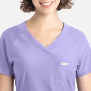 A lilac Y-neck top with a pocket and a logo, featuring a relaxed fit and short sleeves.