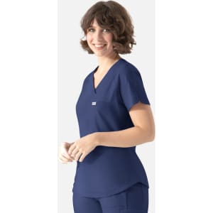 A woman wearing a navy blue Y-neck top with a pocket and a logo. She has short, curly hair and is smiling.