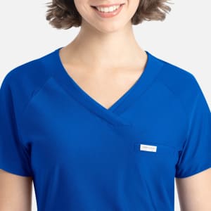 A close-up of a woman's blue Y-neck top with a pocket and branding label. The fabric appears smooth and comfortable.