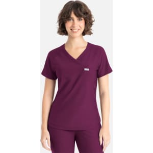 A woman is wearing a plum-coloured Y-neck top with short sleeves and a small logo on the chest.
