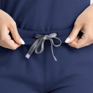 A pair of navy mid-rise joggers featuring a drawstring waistband, held by hands. The joggers have a subtle logo detail.
