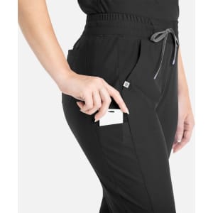A pair of black tapered leg pants with pockets, featuring a drawstring waist and a logo branding detail.