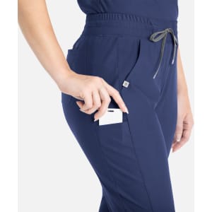 A pair of navy tapered leg pants with a pocket, featuring a person placing a card into the pocket.