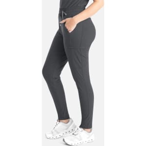 A tapered leg pant in dark grey with pockets, worn by a person. The outfit is complemented by white sneakers.