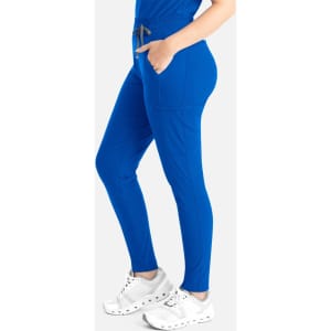 A woman in royal blue tapered leg pants with pockets, paired with white sneakers, stands against a plain background.