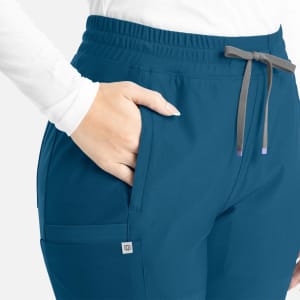 A pair of teal bootcut pants featuring an elastic waistband and pockets, with a branding logo visible.