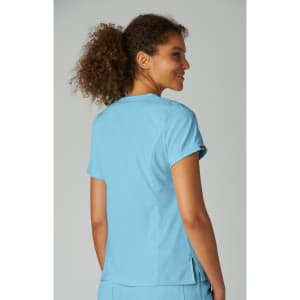 A woman with curly hair wearing a light blue top, featuring a logo on the sleeve, facing away from the camera.