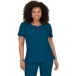 A woman wearing a teal medical scrub top with a round neckline and two front pockets. The top features a logo.