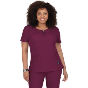 A woman wearing a short-sleeved scrub top in deep burgundy with a round neckline and pockets. The top has a logo.