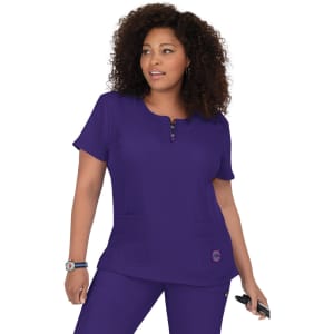 A purple medical scrub top with a round neckline, short sleeves, and two front pockets. The top features a logo.