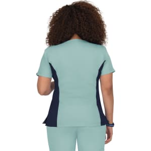 A back view of a turquoise scrub top featuring navy side panels and short sleeves. The garment has a branding logo.