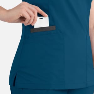 A women's double V-neck top in teal, featuring a side pocket with a card being inserted. It has a discreet logo.