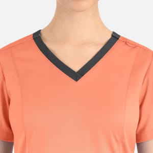 A women's top in coral with a contrast dark grey double V-neck design. Features a small logo on the neckline.