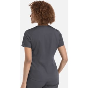 A woman with curly hair wearing a grey tuckable V-neck top, viewed from the back. The top has a logo on the sleeve.