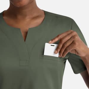 A green women's notched crew neck top with a chest pocket, featuring a hand placing an item inside.